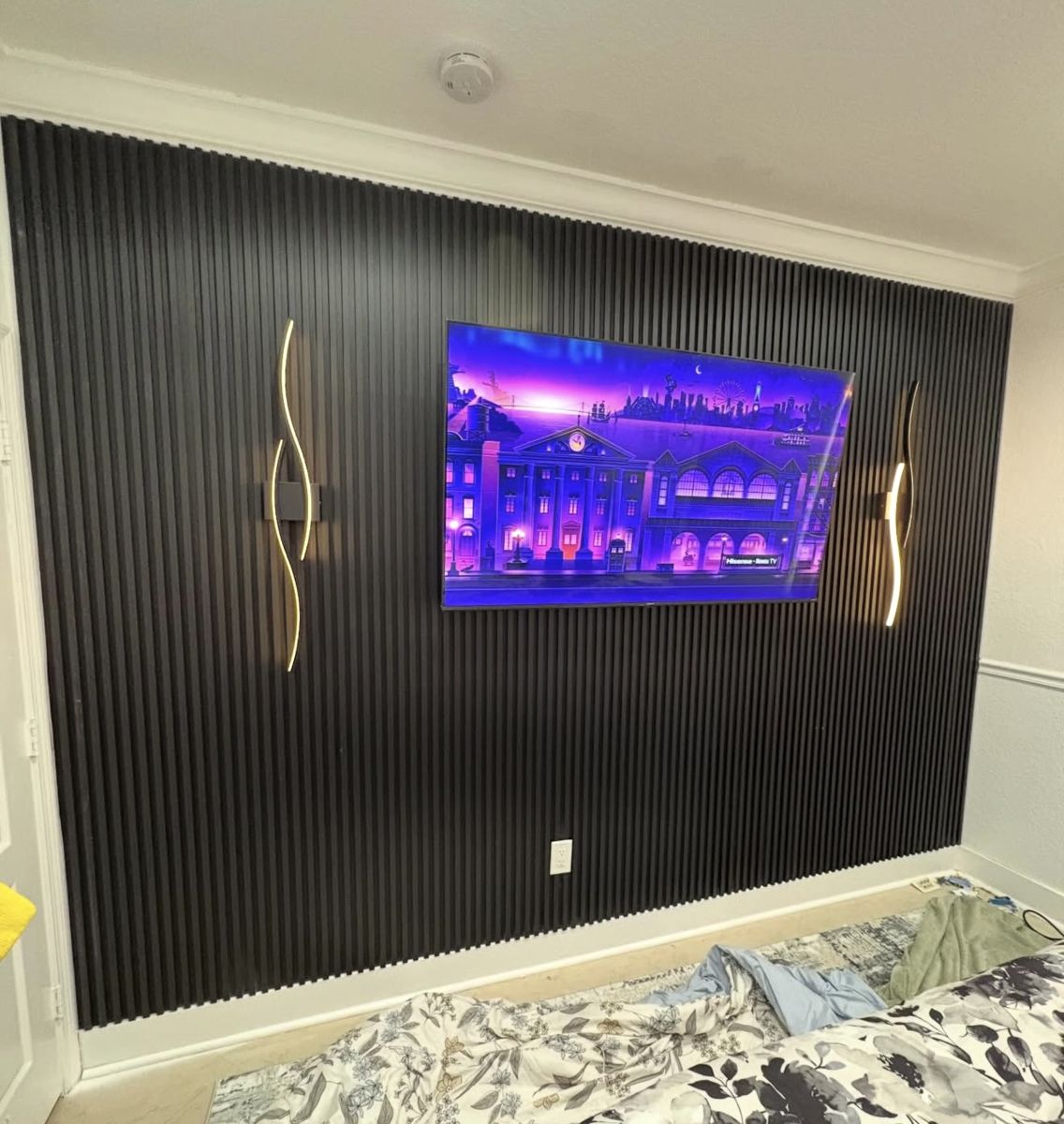 Black slat accent wall with a mounted TV and gold wall lights