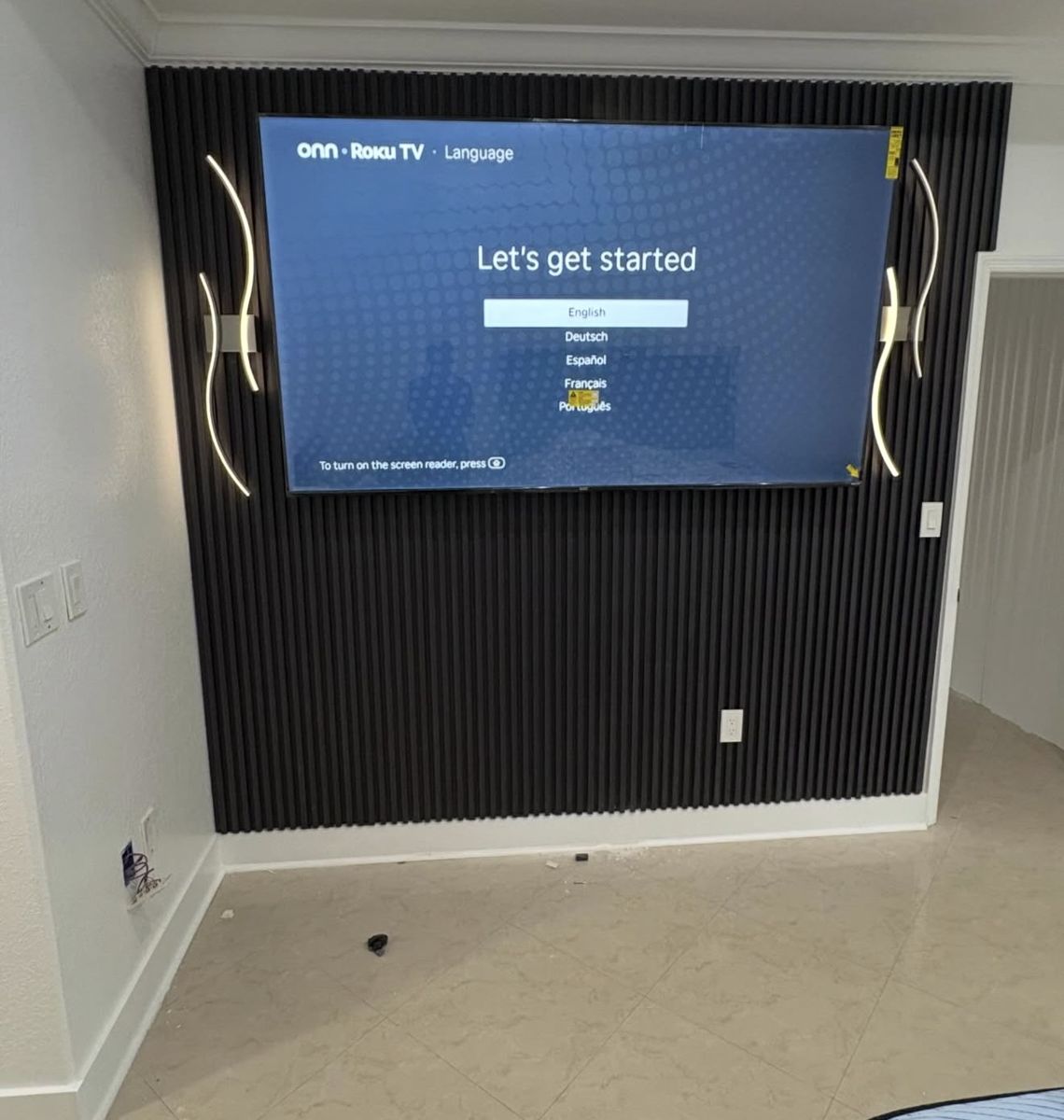 Black slat accent wall with a large TV mounted in a bedroom